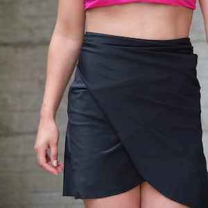 May include: A woman wearing a hot pink bikini top and a black wrap skirt.