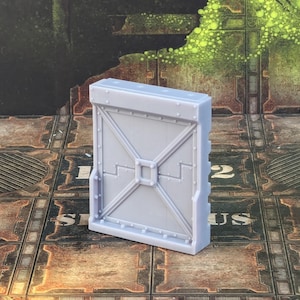Op de afbeelding: Een grijs plastic model van een wandpaneel met een getextureerd oppervlak en een reliëf metalen ontwerp. Het paneel is rechthoekig en ongeveer 15 cm hoog.