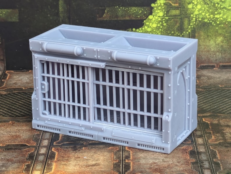 Op de afbeelding: Een grijs, 3D-geprint model van een gevangeniscel met een traliedeur en een klein raam. De cel is ontworpen voor gebruik in een tabletop-spel of een miniatuursetting.