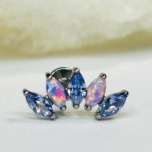 May include: A silver stud earring with a cluster of marquise-cut gemstones. The design features blue and iridescent opal-like stones arranged in a floral or crown-like pattern. The earring is set against a white background.