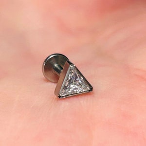 Puede incluir: Un pendiente de aro de plata con un triángulo y un cristal transparente en el centro.