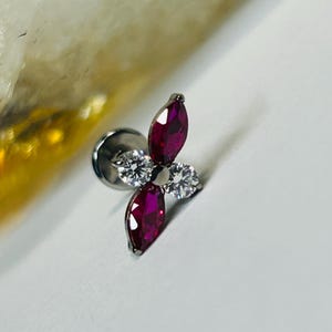 May include: A silver stud earring with a floral arrangement. It features two marquise-cut, deep red gemstones and two round, clear gemstones. The earring is set against a white background.