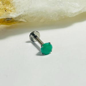 Peut inclure: Une boucle d'oreille à clou argentée avec une pierre précieuse ronde verte vif. La tige de la boucle d'oreille est de couleur argent foncé. La pierre est d'un vert vif et uni.