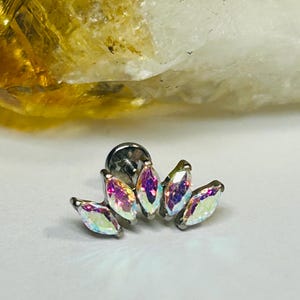 May include: A silver-toned body jewelry piece featuring six iridescent marquise-cut gemstones arranged in a floral or leaf-like design. The gemstones reflect a spectrum of colors, including pink, purple, and green, against a white background.