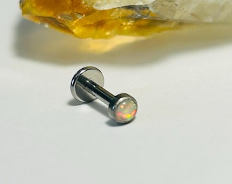 May include: A small, silver-colored labret stud with a flat back and a round, iridescent opal-like stone. The stone displays a range of colors, including pink, yellow, and orange. The jewelry is set against a white background.
