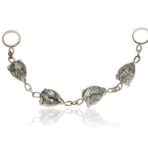 May include: A silver chain bracelet with five irregularly shaped, grey gemstones. The gemstones have dark, linear inclusions and are linked by small silver links. The bracelet has a reflective surface.
