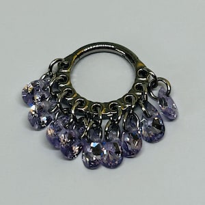 May include: A silver-toned ring with dangling purple teardrop-shaped crystals. The ring has a circular design with smaller crystals attached around the circumference. The crystals are a light purple color and reflect light.