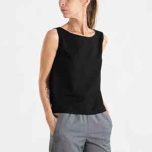 May include: A black sleeveless top with a boat neck and a relaxed fit. The top is paired with grey pinstripe trousers.