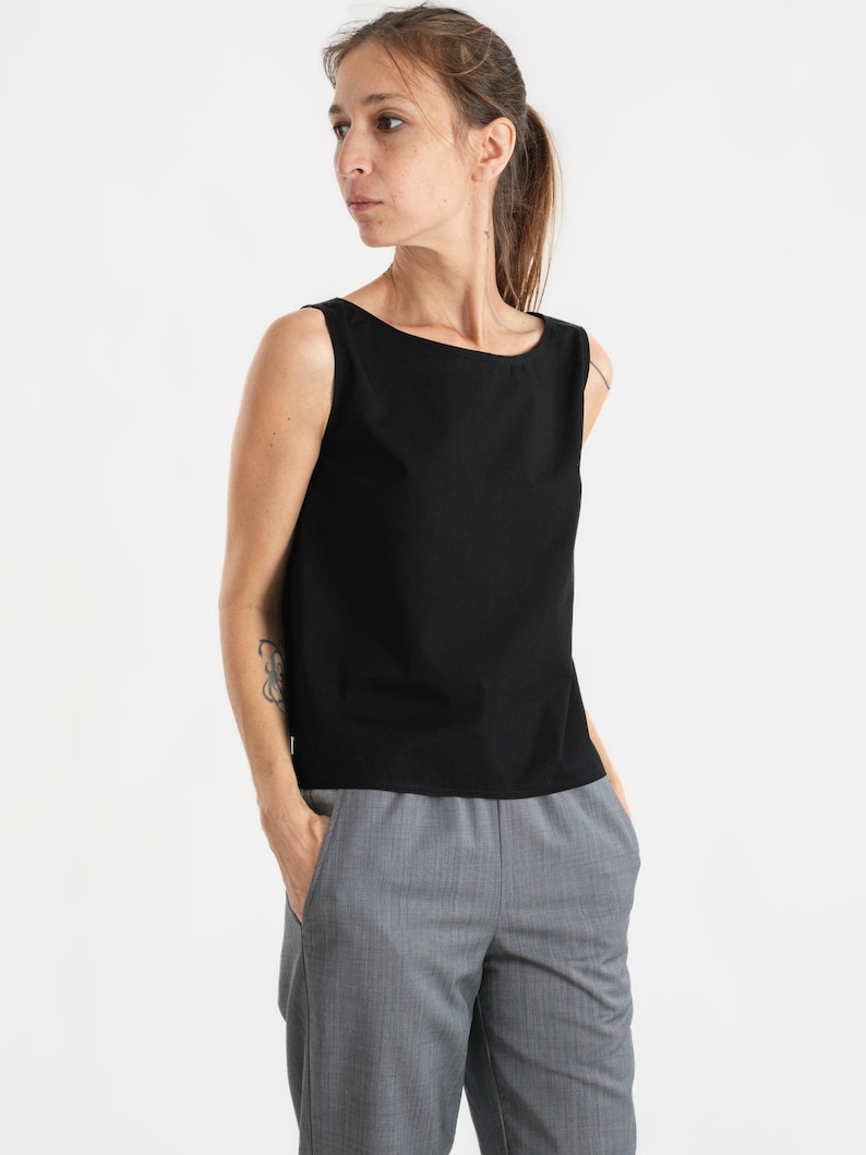 May include: A black sleeveless top with a boat neck and a relaxed fit. The top is paired with grey pinstripe trousers.