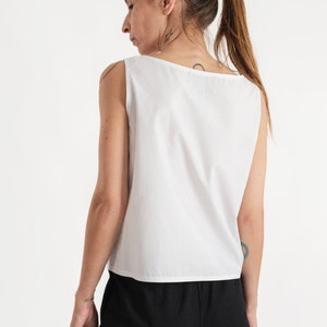 May include: A white sleeveless top with a scoop neck. The top is made of a lightweight fabric and has a relaxed fit.