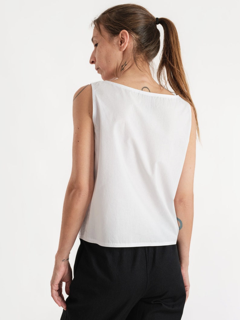 May include: A white sleeveless top with a scoop neck. The top is made of a lightweight fabric and has a relaxed fit.