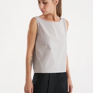 May include: A sleeveless, light grey, scoop neck top with a zip detail on the side. The top is cropped and has a relaxed fit.
