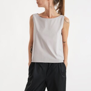 May include: A light grey sleeveless top with a boat neck and a relaxed fit. The top is paired with black trousers with a subtle pinstripe pattern.