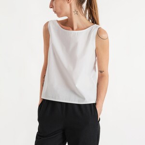 May include: A white sleeveless top with a boat neck and a relaxed fit. The top is paired with black trousers.