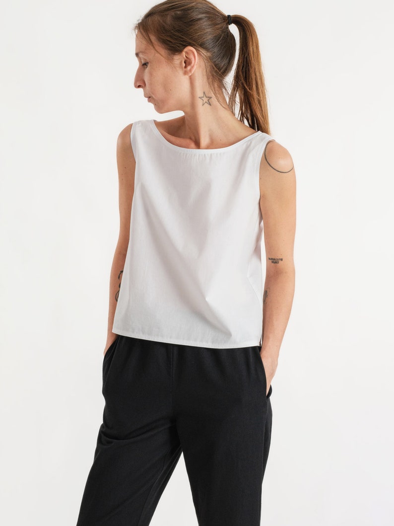 May include: A white sleeveless top with a boat neck and a relaxed fit. The top is paired with black trousers.