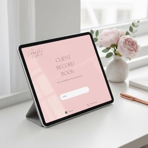 Può includere: Un tablet digitale che mostra uno schermo rosa con il testo "CLIENT RECORD BOOK FOR LASHBROW PROFESSIONALS." Il tablet è appoggiato su una superficie bianca, accanto a un vaso di fiori rosa e una penna color oro rosa.