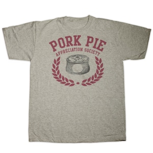 Puede incluir: Una camiseta gris con un gráfico rojo de un pastel de cerdo en una corona con el texto "Pork Pie Appreciation Society".