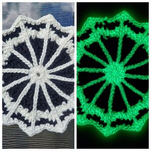 May include: A handmade, crocheted coaster with a starburst design. The coaster features a dark navy blue center with white radiating lines and a scalloped edge. A second image shows the coaster glowing bright green.