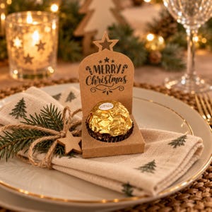 Könnte beinhalten: Ein brauner Papphalter mit einem Sternausschnitt an der Oberseite, der den schwarzen Schriftzug Merry Christmas und Zuckerstangenmotive zeigt. Eine goldverpackte Ferrero Rocher Praline sitzt in der Mitte des Halters auf einer beigen Serviette.