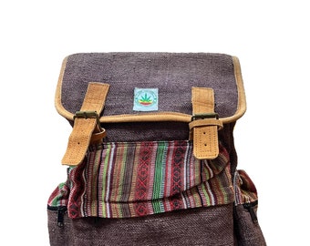 Könnte beinhalten: Ein brauner Hanfrucksack mit einem mehrfarbigen, gestreiften Stoffpanel und Lederriemen. Der Rucksack hat eine kleine Tasche auf der Vorderseite und eine Reißverschlusstasche an der Seite. Der Rucksack hat ein grünes Blattlogo auf der Vorderseite.