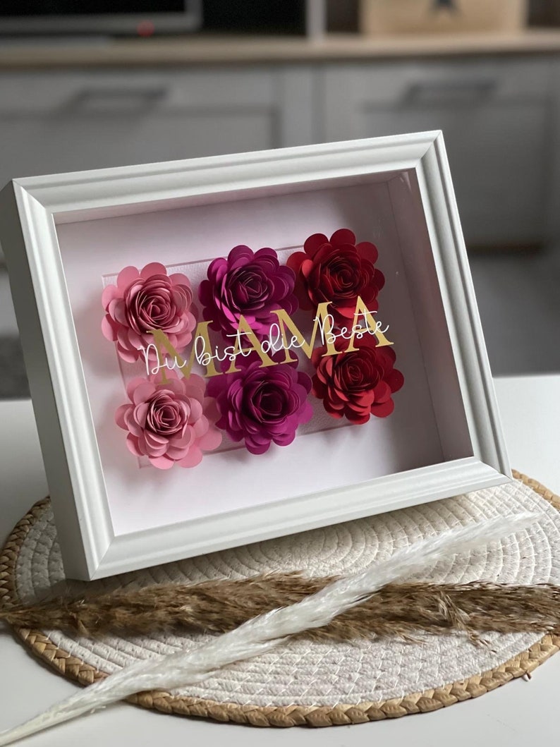 Bilderrahmen mit Papierrosen in Rosa und Rot und einen goldenen Schriftzug mit dem Wort Mama
