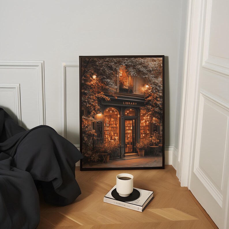 May include: Framed art print depicting a cozy library entrance with the word "LIBRARY" above the door. The print is in a dark frame and is propped against a wall. A white coffee cup sits on a book on the floor.