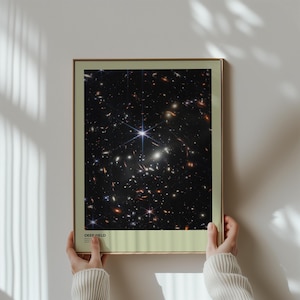 May include: A framed print of a black and white photograph of a deep field of stars. The print has a light green border and the text "DEEP FIELD" at the bottom.