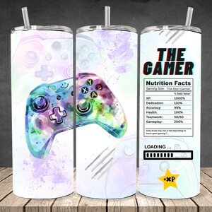 May include: A white 20 oz tumbler with a watercolor design of a video game controller in shades of blue, purple, and green. The tumbler features the text "THE GAMER" and a nutrition facts label with gaming-related stats.