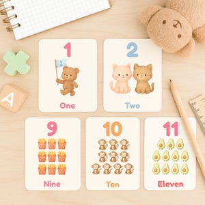 May include: Educational flashcards featuring numbers 1, 2, 9, 10, and 11. Each card displays a number with corresponding illustrations of a bear, cats, french fries, monkeys, and avocados. The word for each number is also printed.