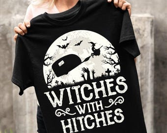 May include: Black t-shirt with a white graphic of a witch flying on a broomstick in front of a full moon with a camper in the foreground. The text "Witches with hitches" is below the graphic.
