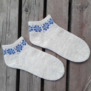 May include: A pair of light gray ankle socks with a blue floral pattern at the cuff. The socks are made of a soft, knitted material and are displayed on a wooden surface.