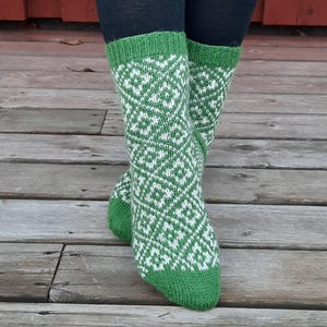 May include: A pair of green and white patterned socks. The socks feature a geometric design in white against a green background. The cuffs and toes are solid green. The socks are worn over black leggings.