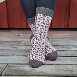 May include: A pair of mid-calf knit socks featuring a repeating geometric diamond pattern in soft pink and dark brown. The socks have a solid dark brown ribbed cuff at the top and a solid dark brown toe section, crafted with a visible knit texture.