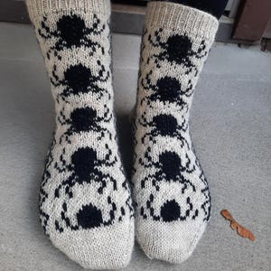 Puede incluir: Calcetines de punto color crema con un patrón repetido de insectos negros. Los calcetines, visibles desde los tobillos, muestran el diseño detallado y la textura. Fabricados con un material suave y cálido, ideales para el invierno.