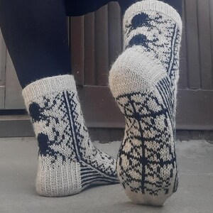 Puede incluir: Un par de calcetines de punto en una combinaci&oacute;n de colores gris claro y azul marino. Los calcetines presentan un patr&oacute;n repetitivo en forma de &aacute;rbol y detalles en azul oscuro. Los pu&ntilde;os y los talones son de color gris claro liso.
