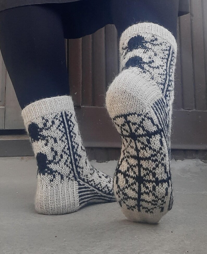 Puede incluir: Un par de calcetines de punto en una combinaci&oacute;n de colores gris claro y azul marino. Los calcetines presentan un patr&oacute;n repetitivo en forma de &aacute;rbol y detalles en azul oscuro. Los pu&ntilde;os y los talones son de color gris claro liso.