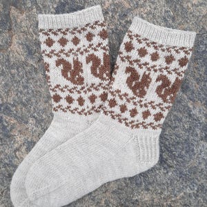 May include: A pair of knitted socks in light gray with a brown squirrel and diamond pattern. The socks are made of a soft, textured material and are designed to keep feet warm. The socks are a cozy accessory.