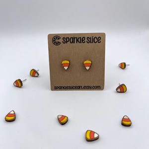 May include: A pair of wooden candy corn earrings with orange, yellow, and white paint. The earrings are on a card with the text "Sparkle Slice" and "sparklesliceart.etsy.com".