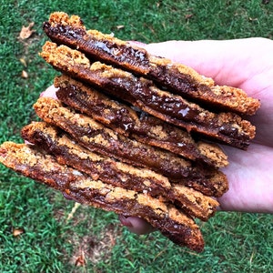 May include: A stack of six chocolate chip cookies with a layer of melted chocolate between each cookie. The cookies are a light brown color and have a slightly crispy texture.