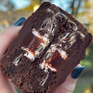 May include: A chocolate brownie with a layer of white frosting and a mint chocolate chip filling, cut in half and held in a hand.