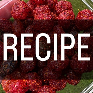 Puede incluir: Primer plano de un bol lleno de fresas rojas secas y azucaradas. Las fresas están cubiertas de un glaseado rojo azucarado y tienen un aspecto ligeramente picante. La palabra "RECETA" está escrita en letras blancas sobre la imagen.