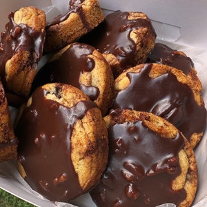 May include: A white box filled with chocolate-covered cookies. The cookies are a light brown color and have a swirl pattern. The chocolate is a dark brown color and is smooth and glossy.