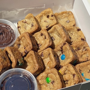 May include: A white box filled with small square chocolate chip cookies, some with colorful M&M's. Two small clear containers with chocolate dipping sauce are included.