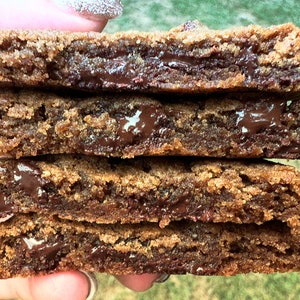 May include: A stack of four chocolate chip cookies, each with a layer of melted chocolate in the middle. The cookies are brown and have a slightly crispy texture.