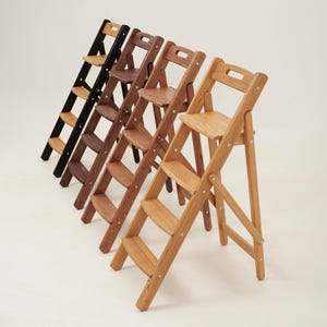 Peut inclure: Plusieurs escabeaux pliants en bois de différentes teintes de marron et de noir. Chaque escabeau comporte trois marches et une petite assise. Les escabeaux sont posés sur un fond blanc.