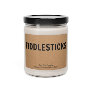 May include: A glass jar candle with a brown paper label that reads "FIDDLESTICKS" and "9oz Soy Candle Vegan | Natural | Non-Toxic".