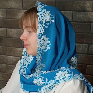 以下が含まれることがあります： 縁に白い花の刺繍が施された鮮やかなターコイズのヘッドカバー。 ヘッドカバーは頭と肩にかけられ、柔らかく流れるような効果を生み出しています。 刺繍は詳細な花の模様が特徴です。