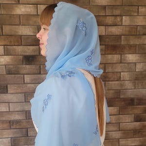 以下が含まれることがあります： スカラップエッジと刺繍された花のディテールが施された、薄い水色のヘッドカバー。透け感のある生地が頭と肩にドレープされています。刺繍は、お揃いの水色です。