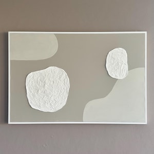 May include: A framed abstract painting with a beige background and white textured shapes. The shapes are organic and resemble clouds.
