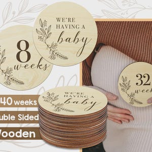May include: Wooden, double-sided pregnancy milestone discs. One disc reads "8 weeks" with floral accents, another says "We're having a baby." A third disc shows "32 week". The stack of discs shows the text "8-40 weeks".